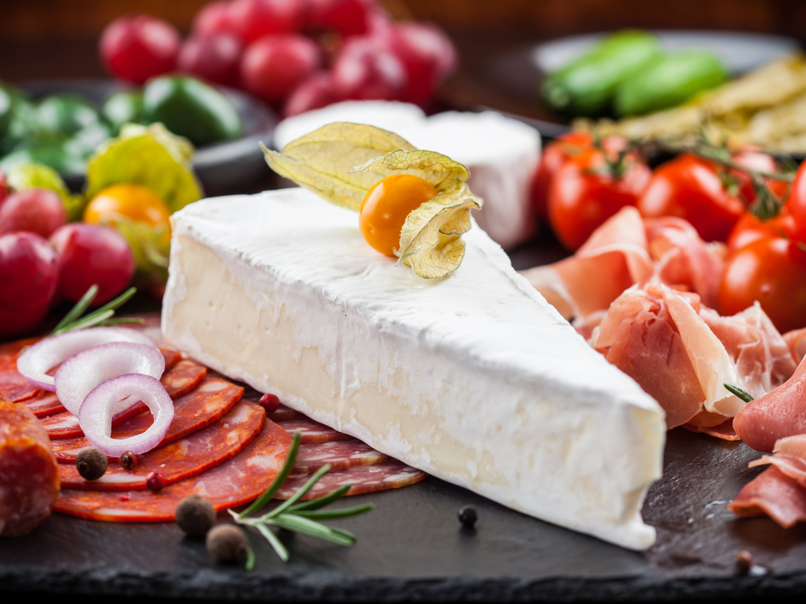 Кусок сыра на столе с овощами и колбасой