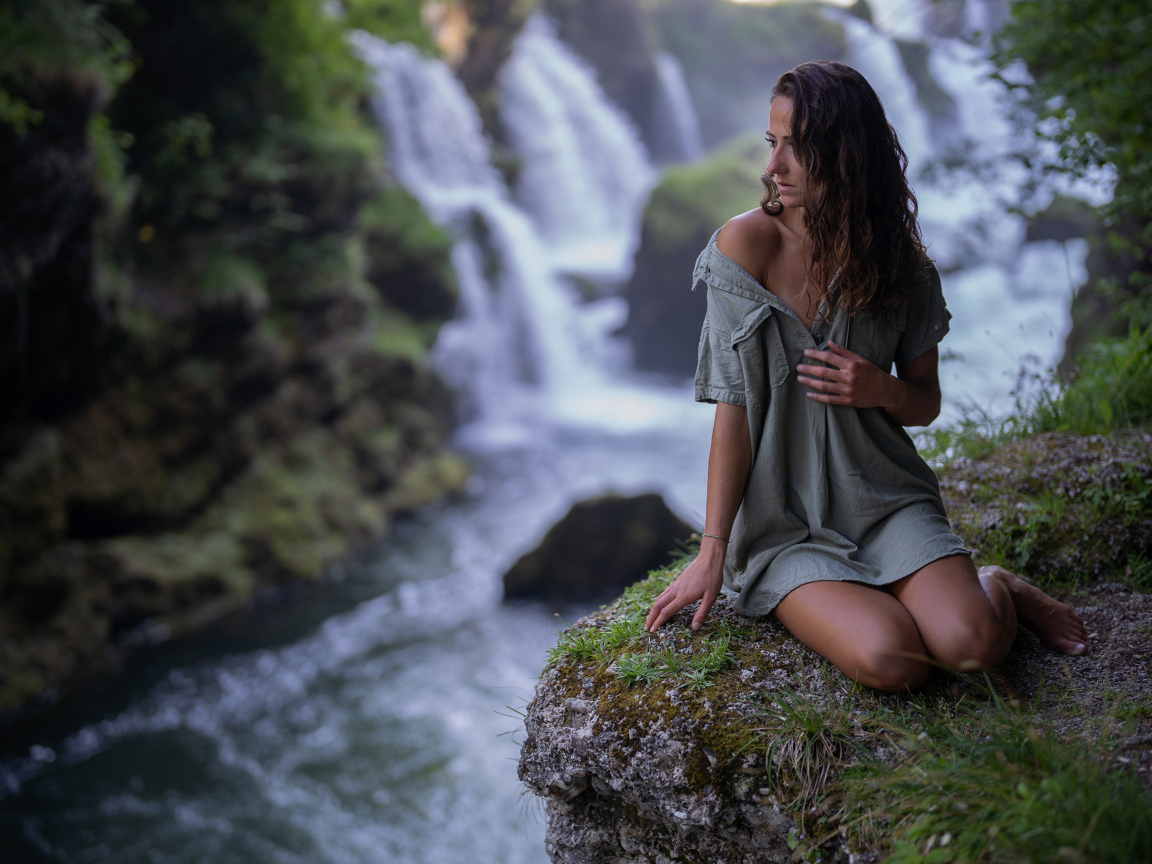 Девушка в рубашке сидит у водопада
