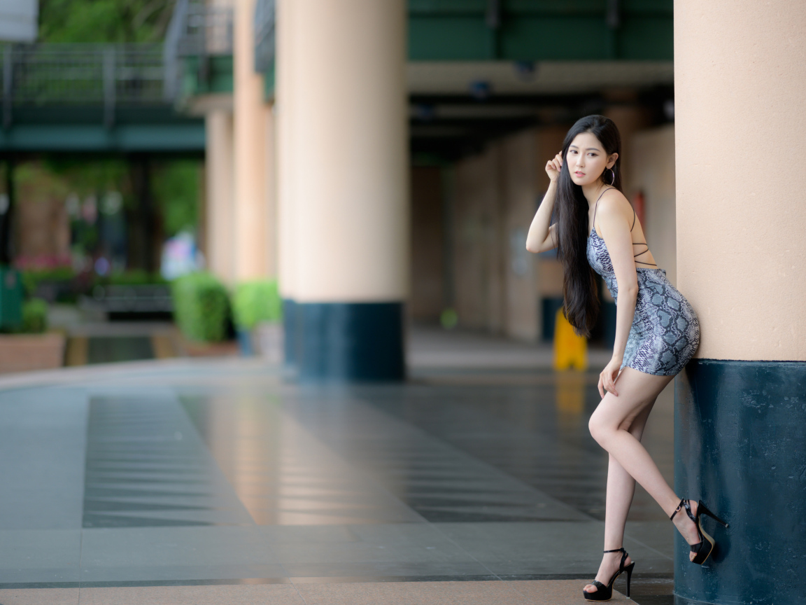 Стройная азиатка в коротком платье  стоит у колонны