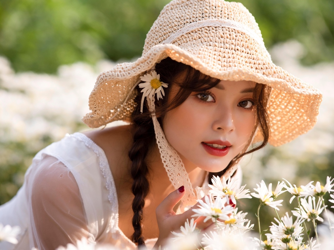 Девушка азиатка в шляпке на поле с ромашками