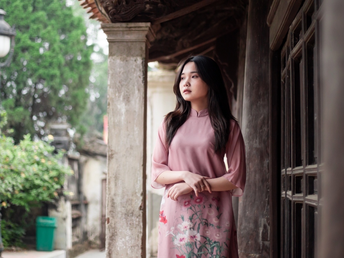 Девушка азиатка в розовом платье стоит у дома