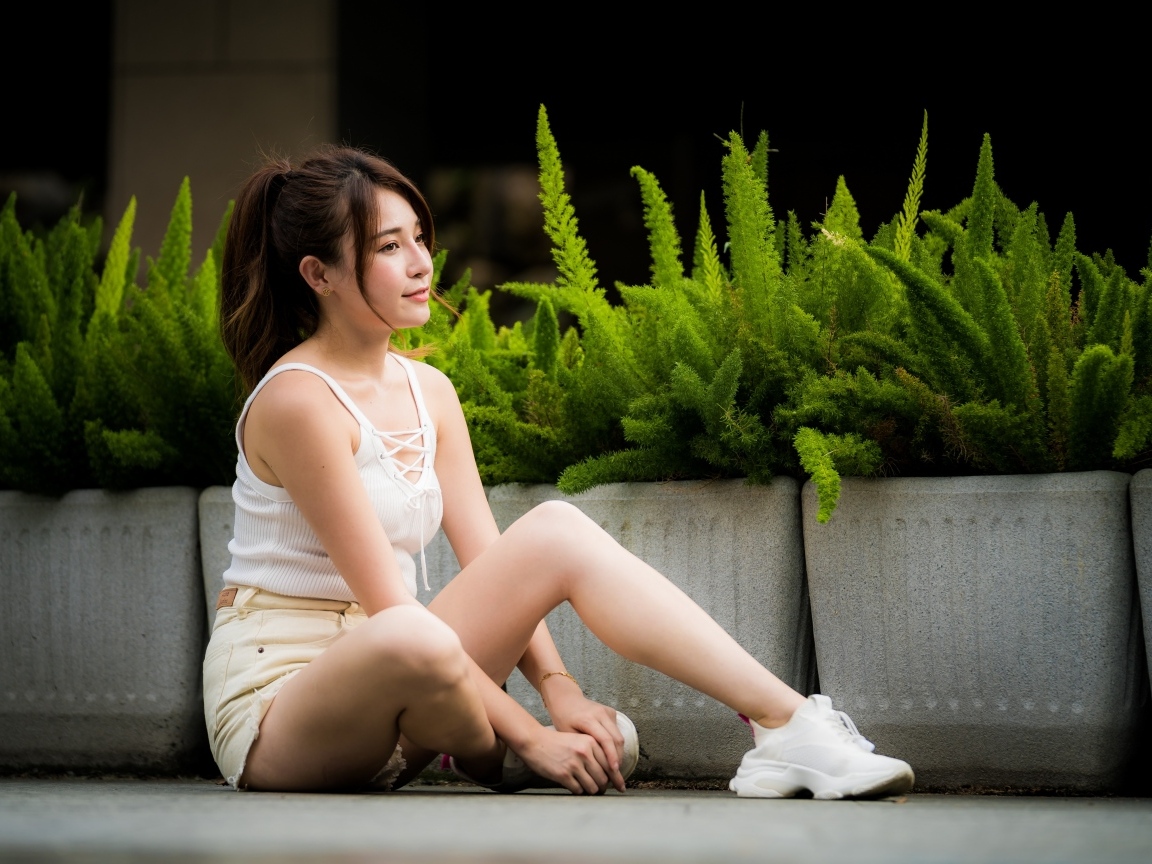 Девушка азиатка сидит на земле у зеленых растений