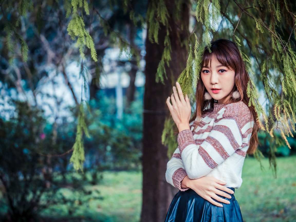 Девушка азиатка стоит у дерева ели