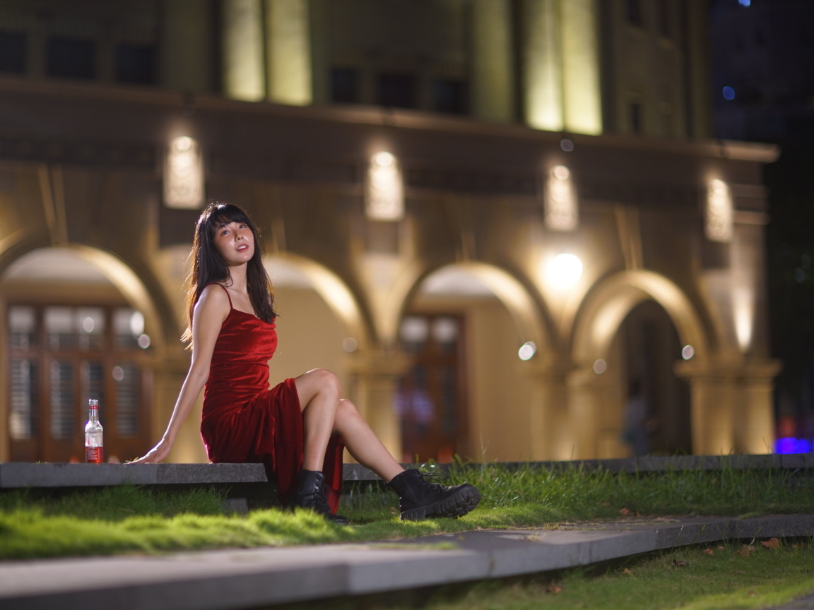 Азиатка в длинном красном платье сидит на ступенях