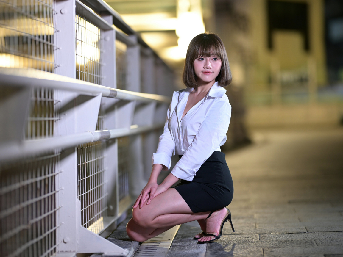 Азиатка в белой блузке и черной юбке сидит на корточках