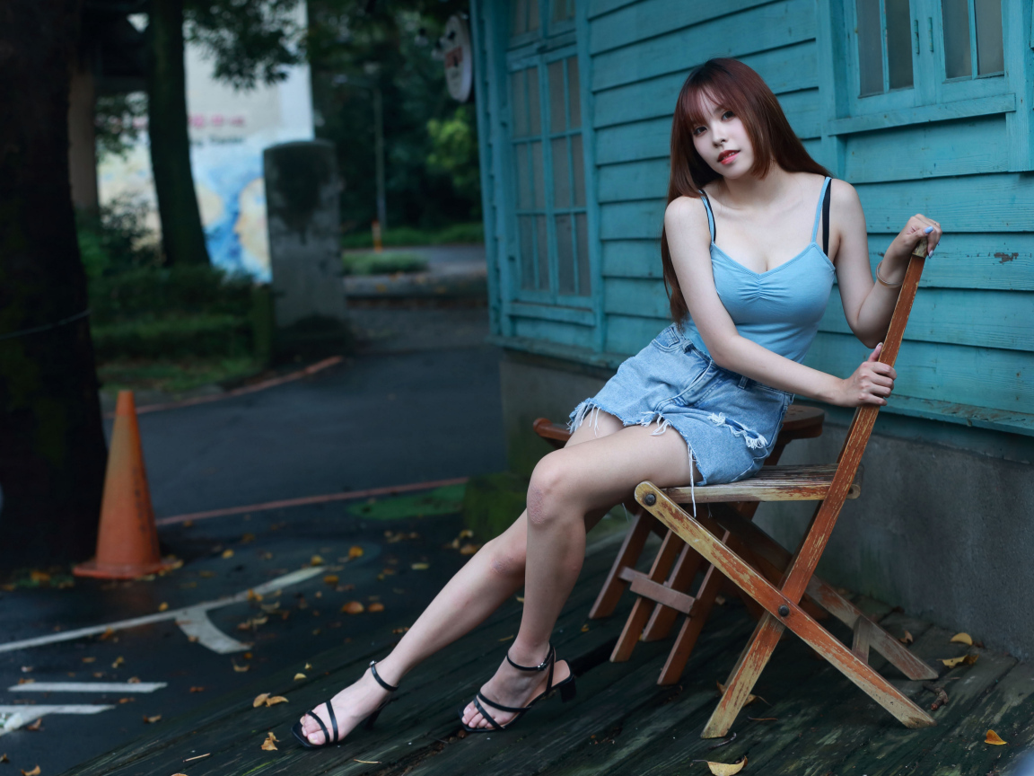 Красивая девушка сидит на стуле у дома