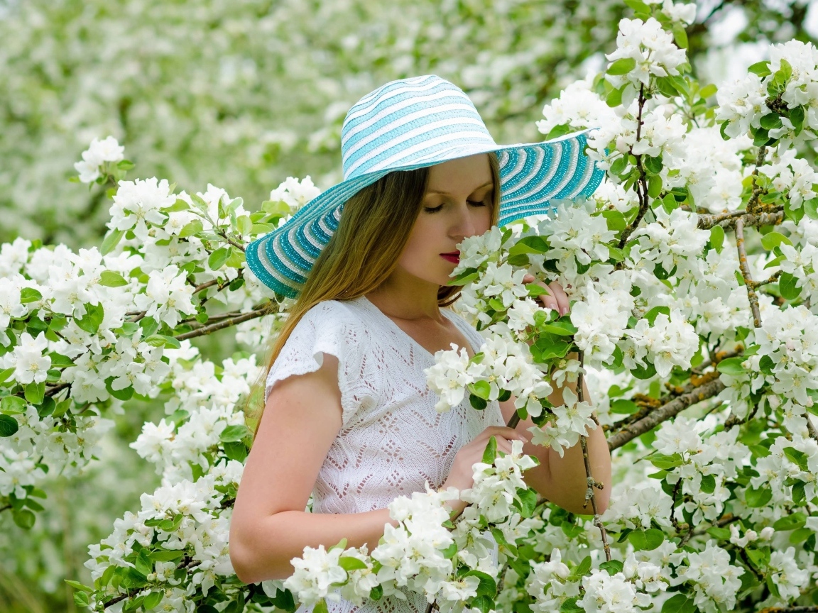 Девушка в шляпе нюхает ветку яблони 