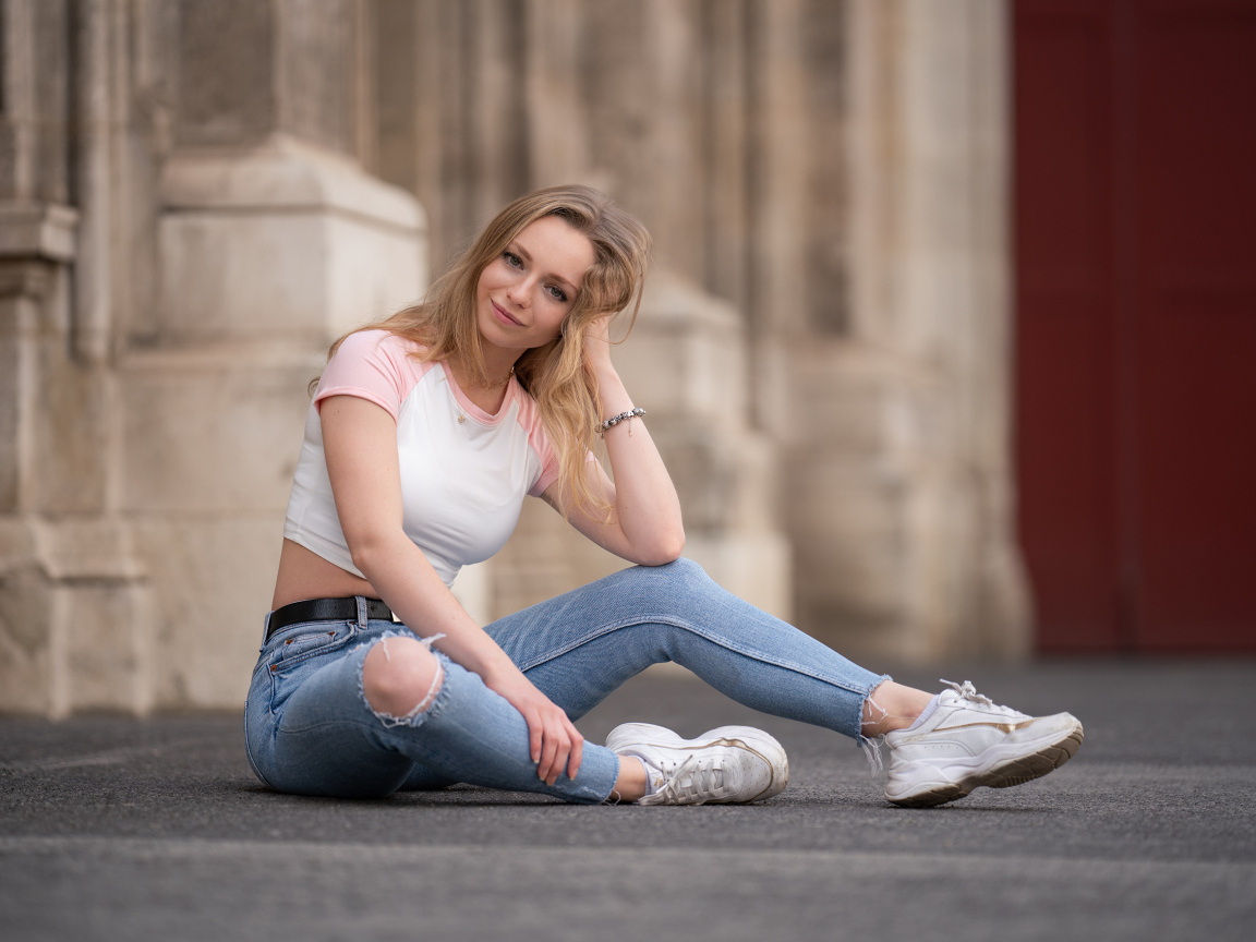 Девушка в рваных джинсах сидит на асфальте