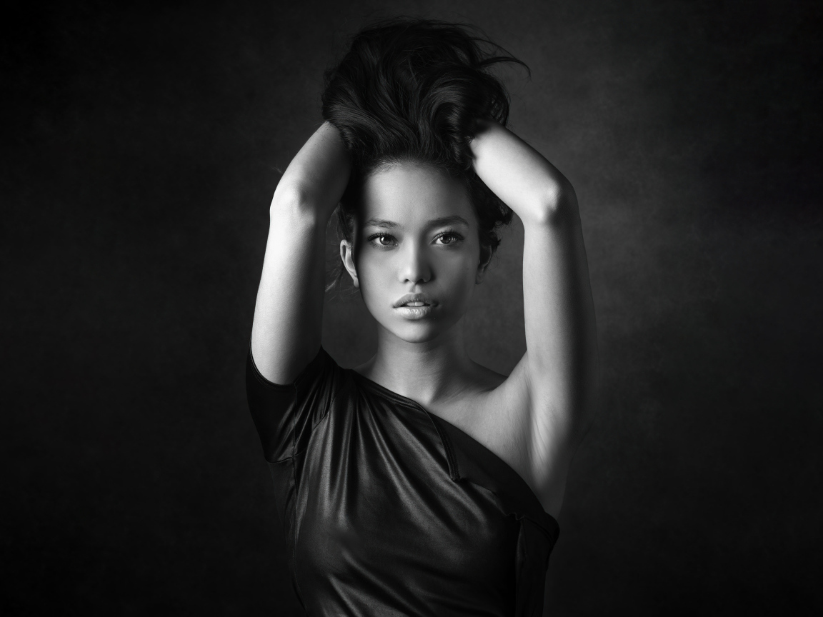 Девушка модель с руками в волосах  у стены