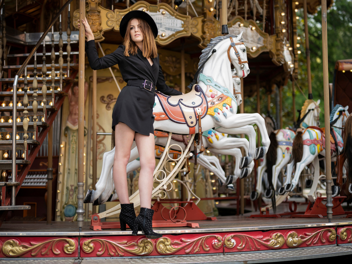 Молодая девушка в черном платье у карусели в парке