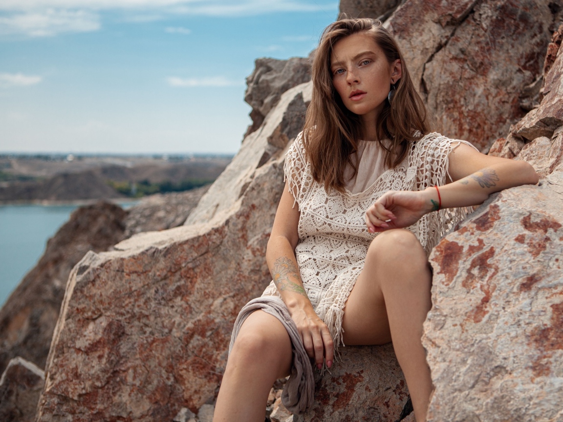 Молодая девушка сидит на камнях