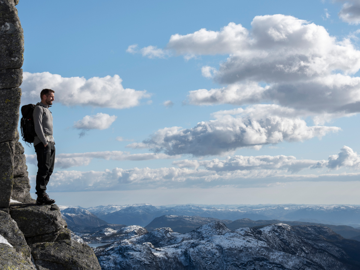 Мужчина стоит на краю скалы на фоне неба 