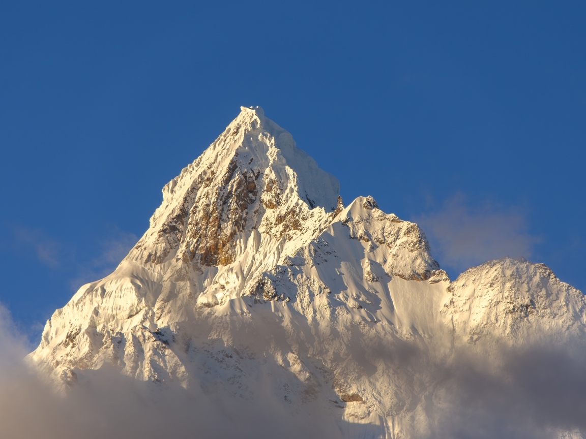 Крутая заснеженная вершина горы на голубом фоне