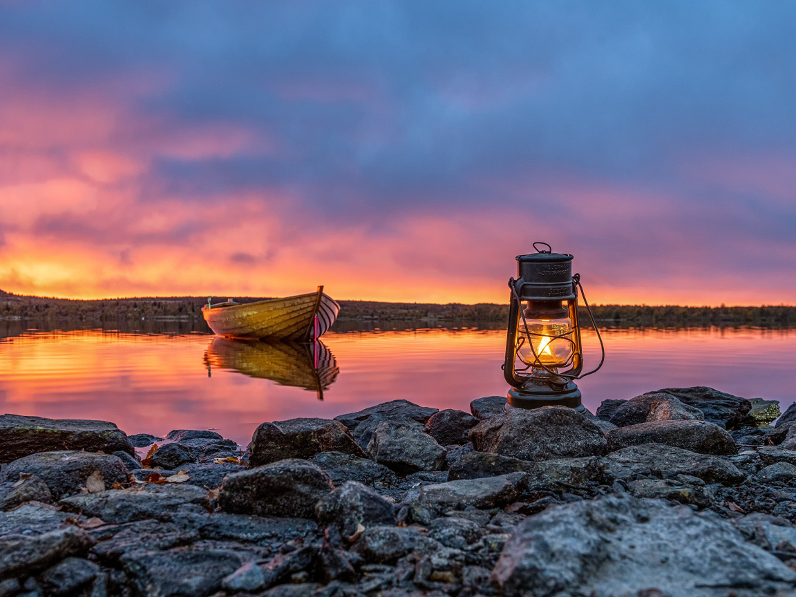 Керосиновая лампа стоит на камнях у озера