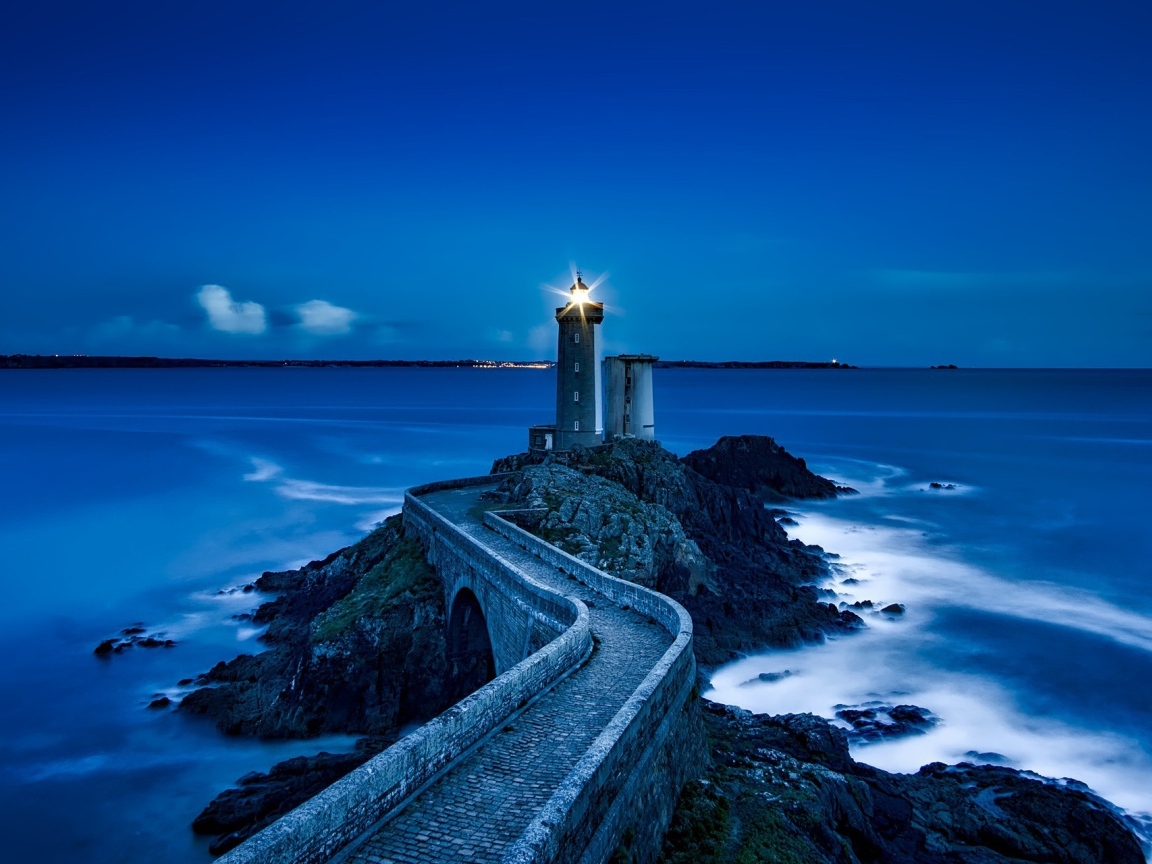 Lighted lighthouse on the seashore at night