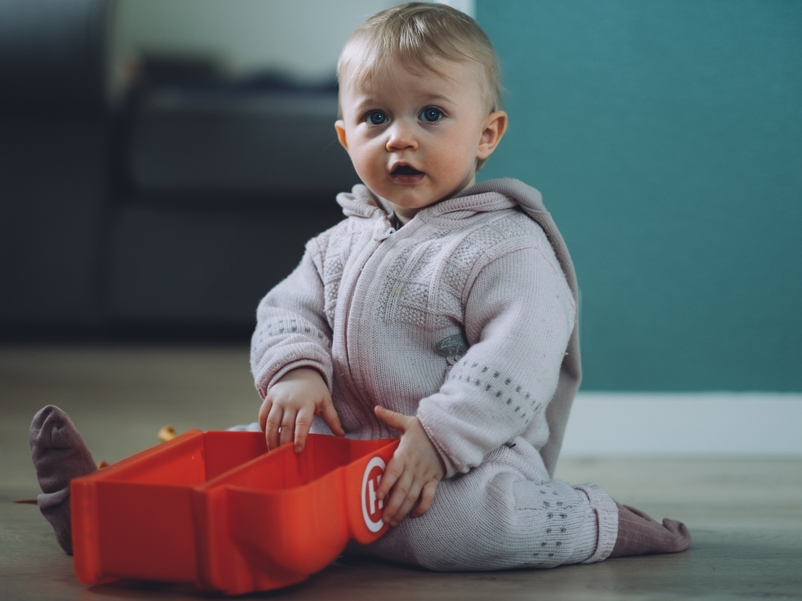 Маленький мальчик в теплом костюме сидит на полу