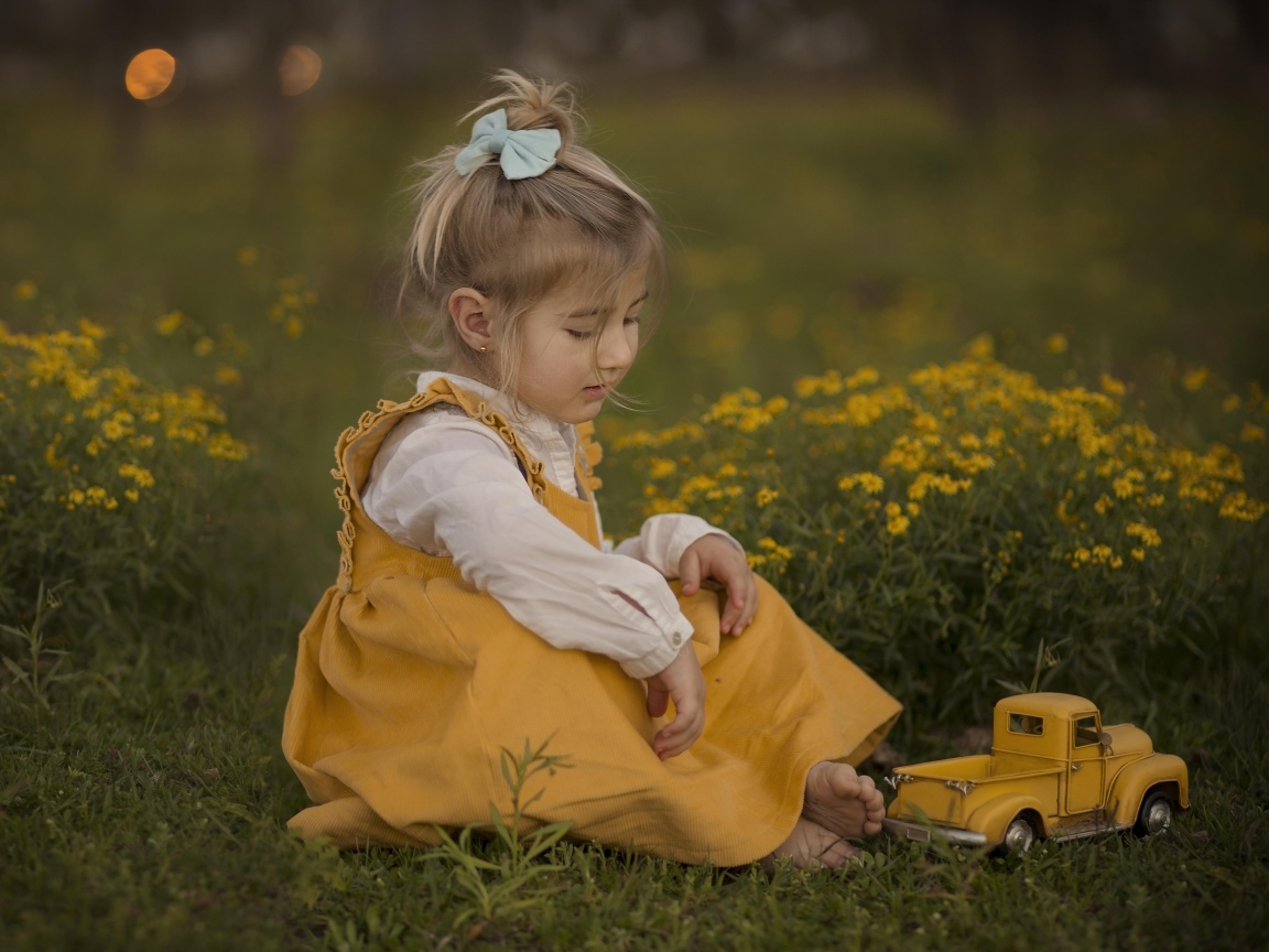 Девочка сидит на траве с игрушечной машинкой