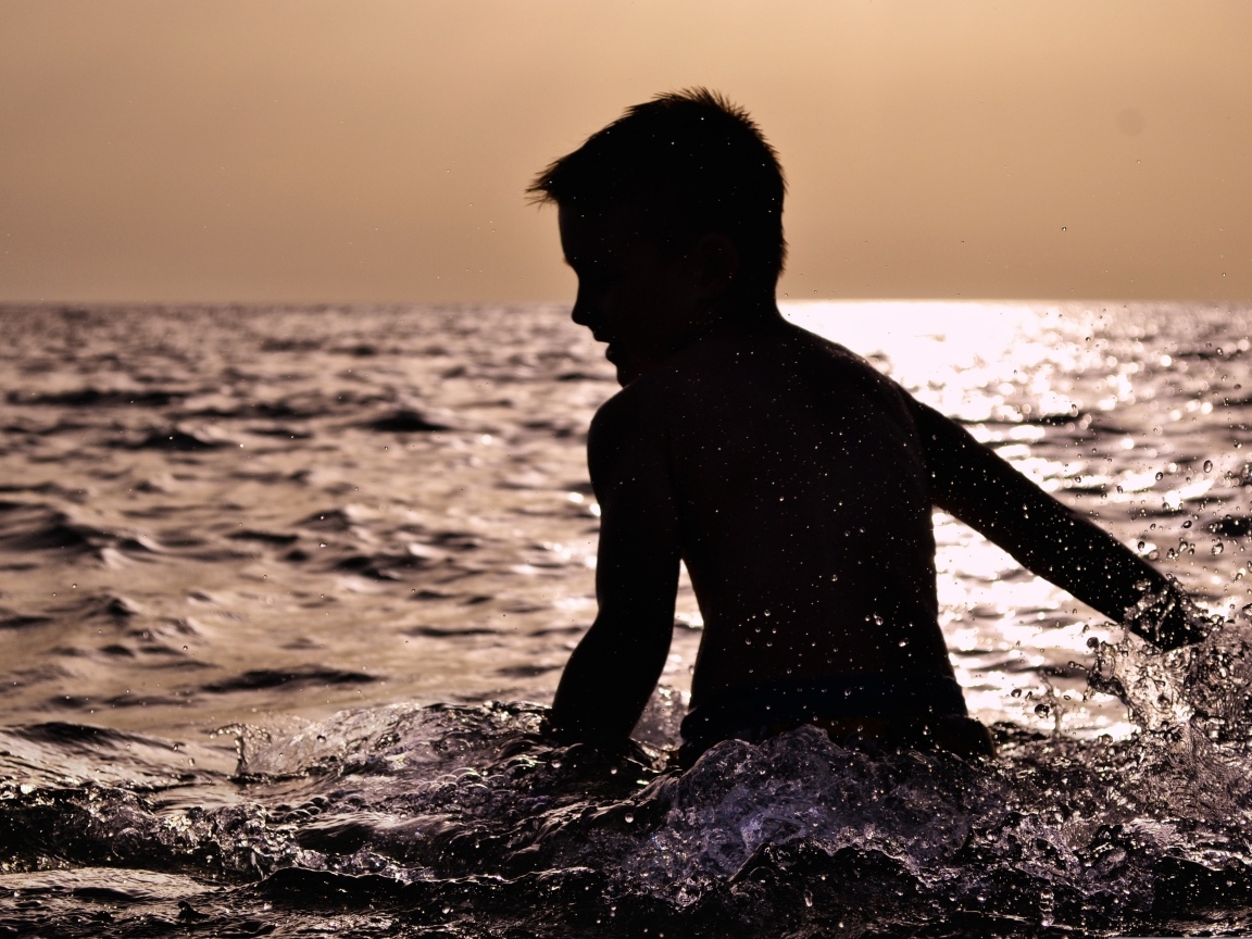 Маленький мальчик купается в воде летом