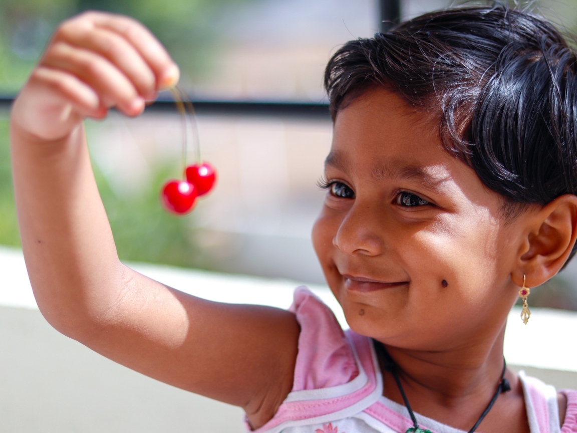 Маленькая улыбающаяся девочка с ягодами вишни в руках