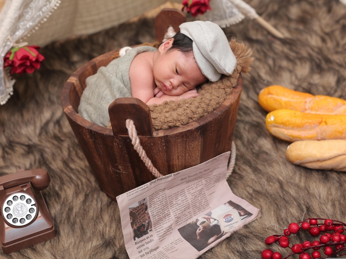Новорожденный маленький мальчик в деревянном ведре на фотосессии 