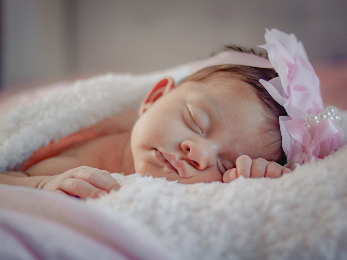 Спящая новорожденная девочка с розовым бантом на голове