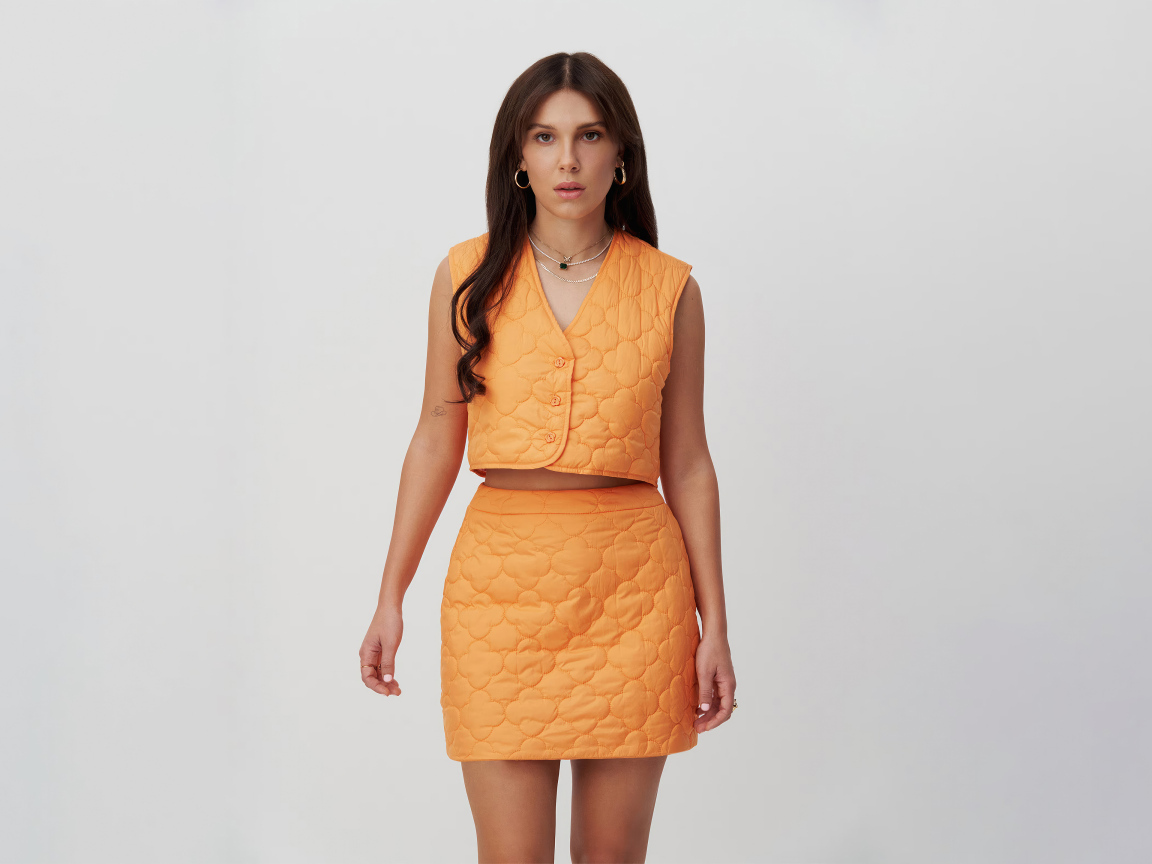 Девушка актриса Милли Бобби Браун в костюме на сером фоне