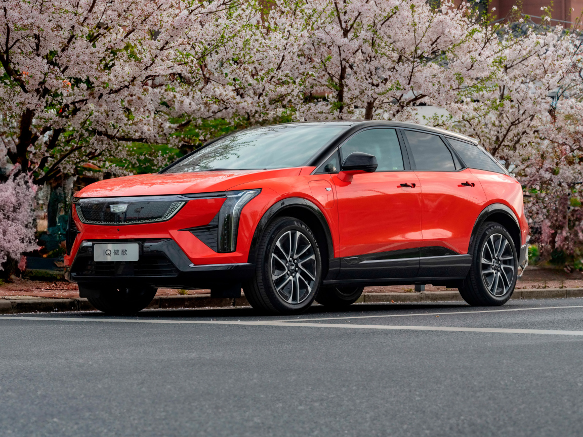 Красный Cadillac Optiq Sport 2024 года у цветущих деревьев
