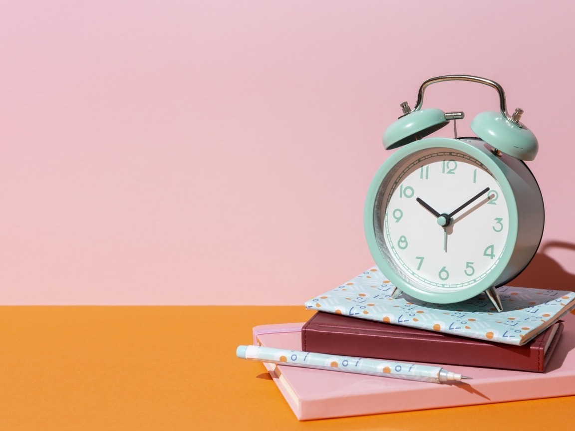 Будильник с книгами на розовом фоне