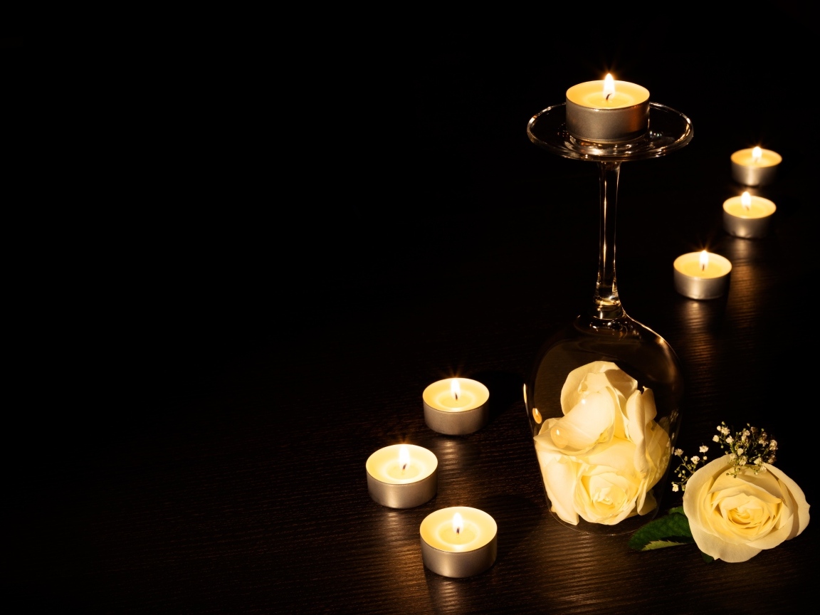 Зажженные свечи с цветами розы на черном фоне