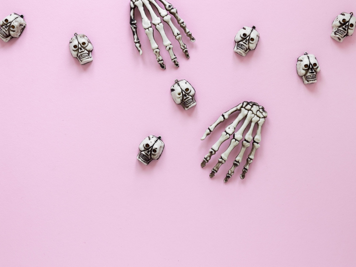 Кисти рук скелета и черепа на розовом фоне
