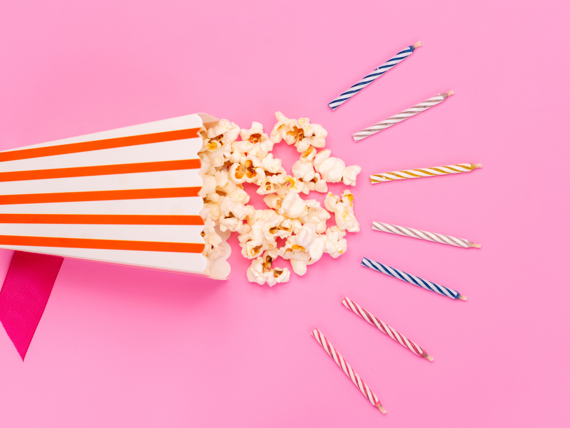Коробка попкорна со свечами на розовом фоне