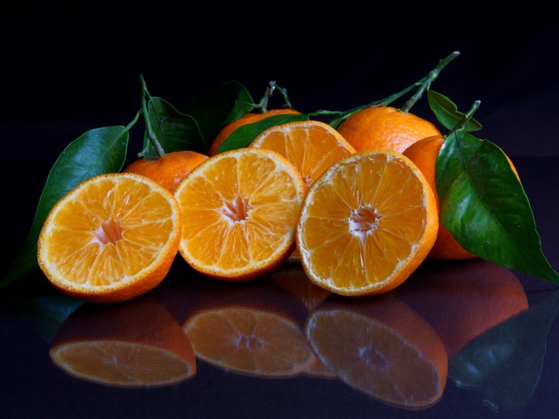 Половинки мандарина с листьями на черной поверхности