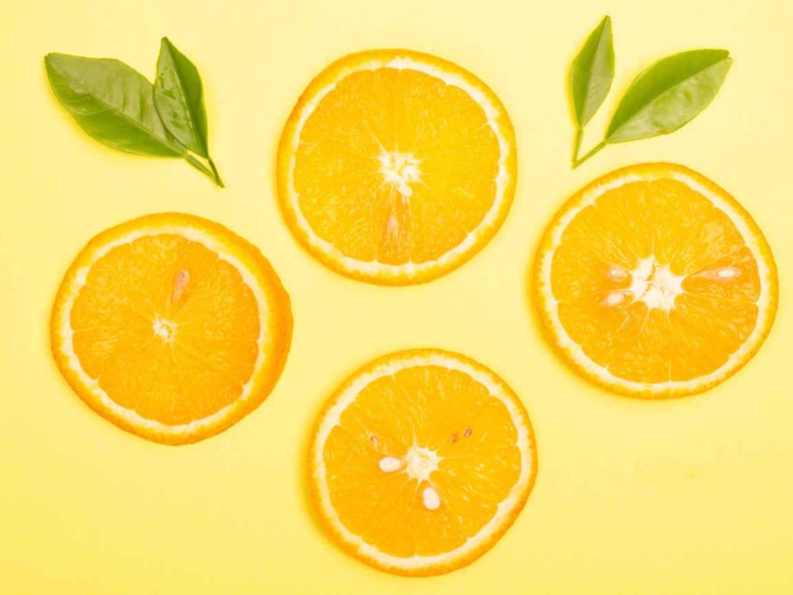 Нарезанный апельсин с зелеными листьями на желтом фоне