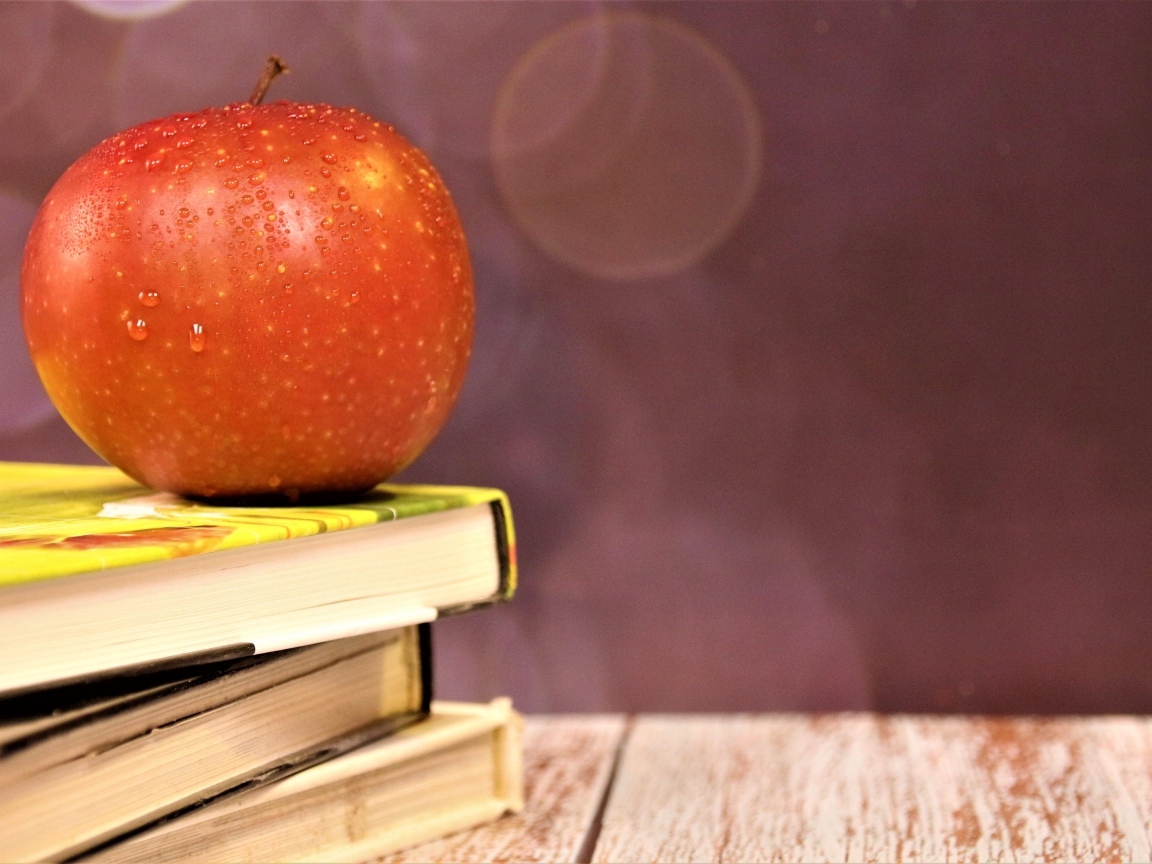 Мокрое яблоко на столе с книгами