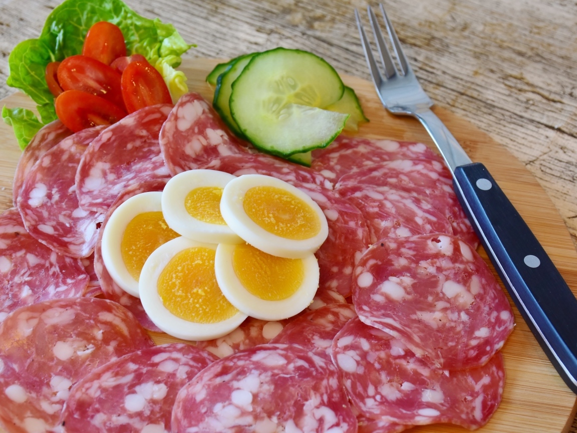 Колбаса салями на доске с вареными яйцами и овощами