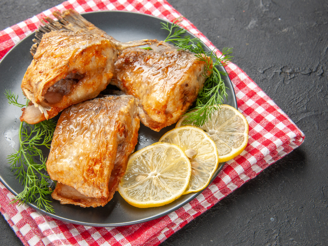 Куски жареной рыбы на тарелке с кусочками лимона и укропом