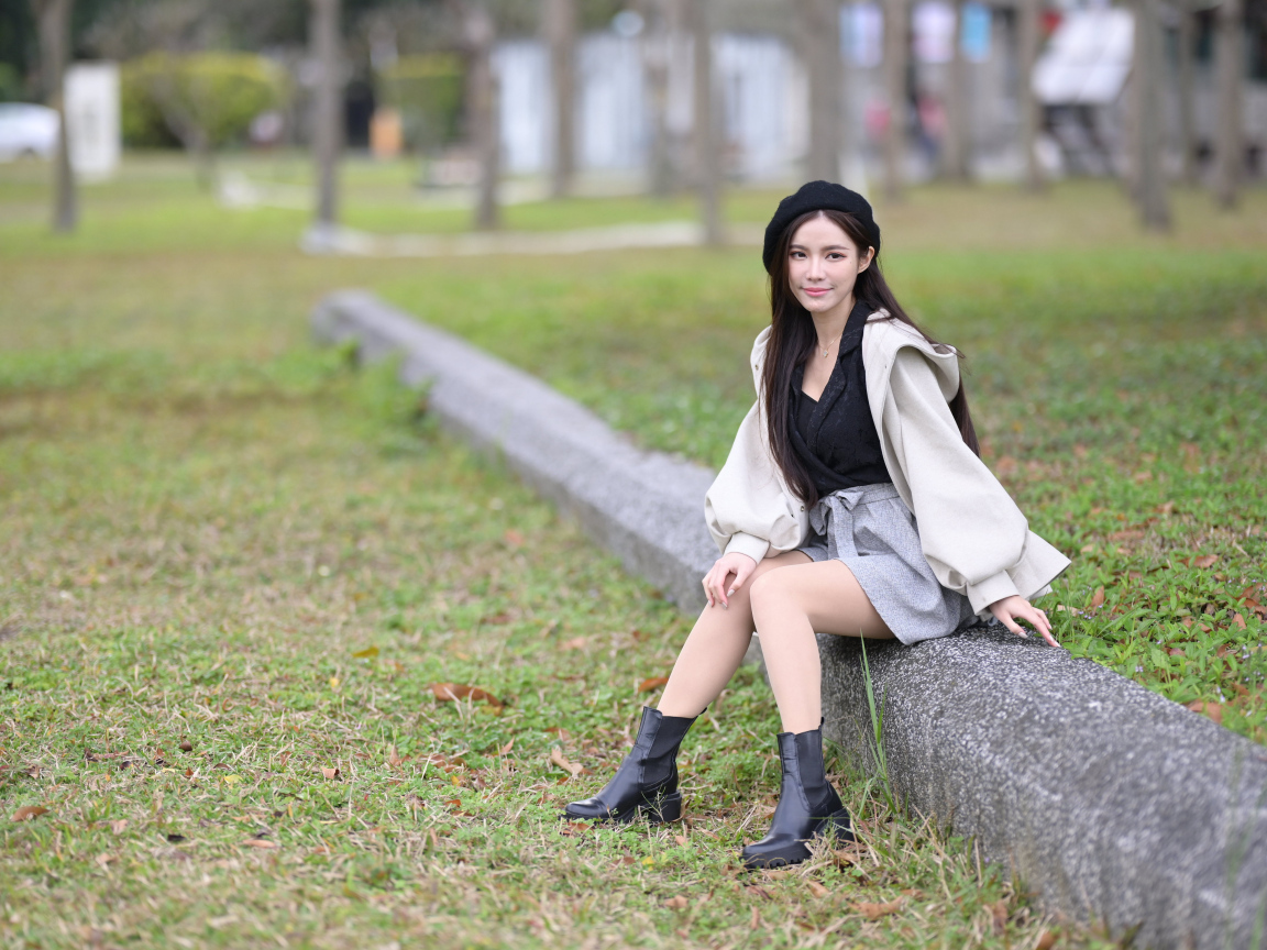 Девушка в пальто сидит на земле в парке