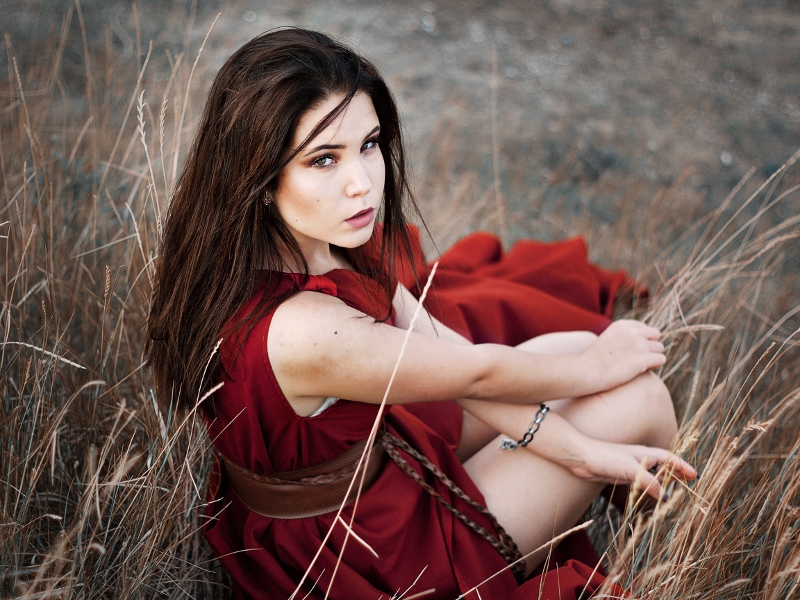 Девушка в красном платье сидит в траве