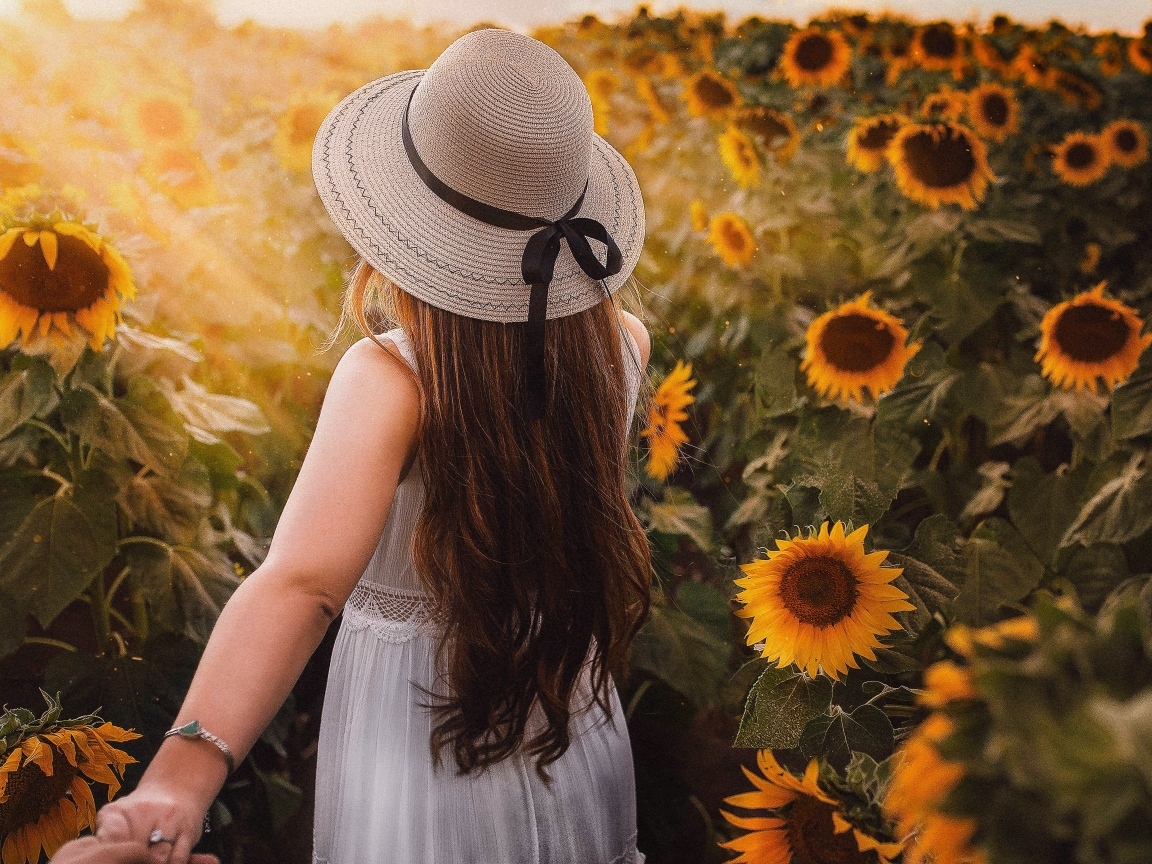 Девушка в белом платье и шляпе идет по полю с подсолнухами