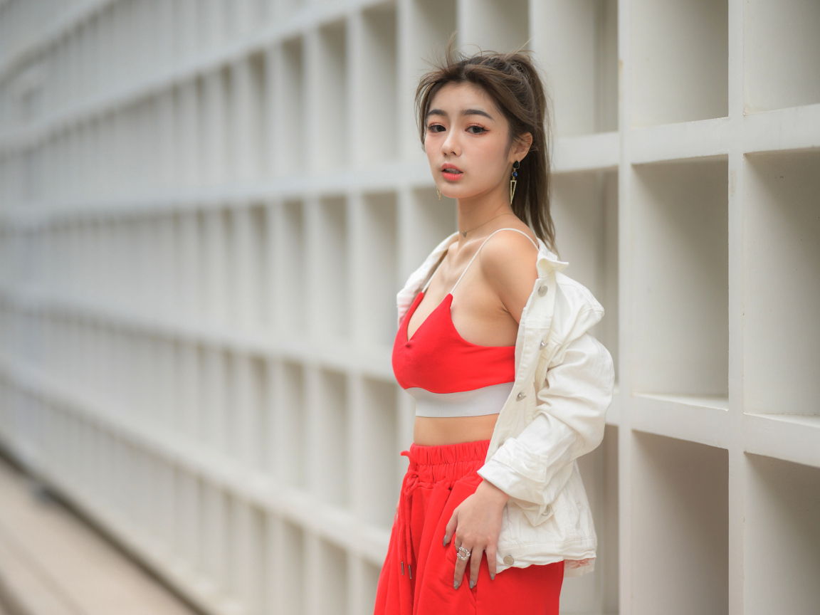 Азиатка в красном спортивном костюме стоит у стены