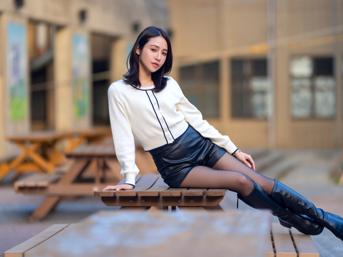 Азиатка сидит на лавке в черных кожаных сапогах