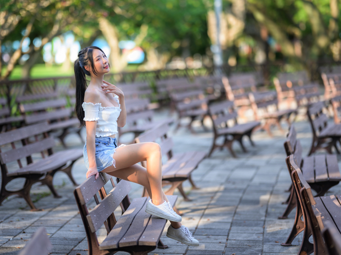 Спортивная азиатка сидит на лавке в парке