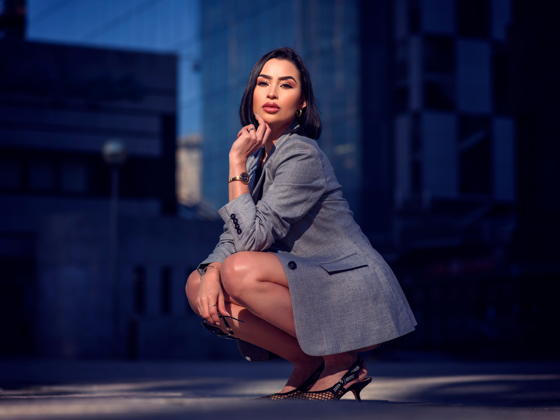 Красивая брюнетка в сером пиджаке сидит на корточках