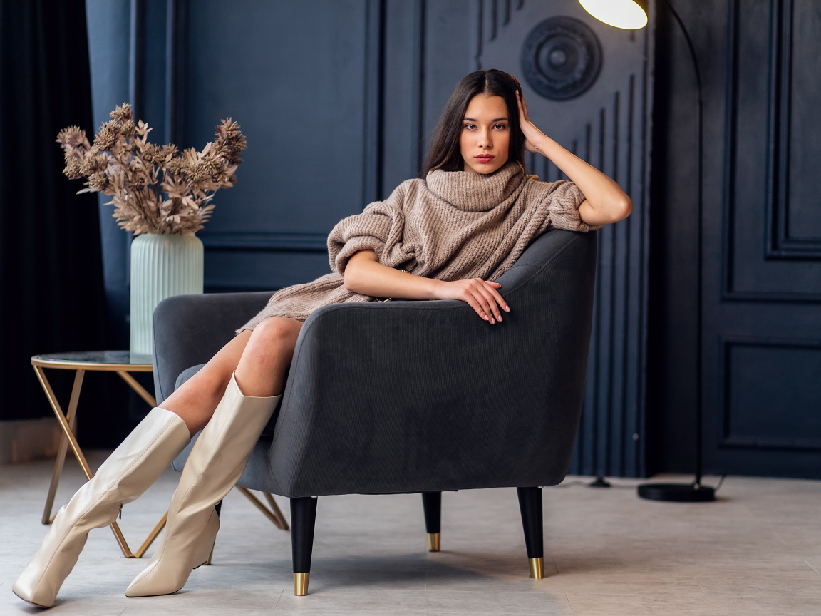 Красивая брюнетка в сапогах сидит в кресле