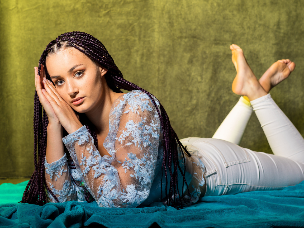 Брюнетка с косами на голове лежит на постели