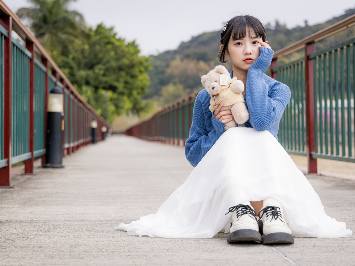 Милая азиатка с игрушечным медвежонком сидит на мосту