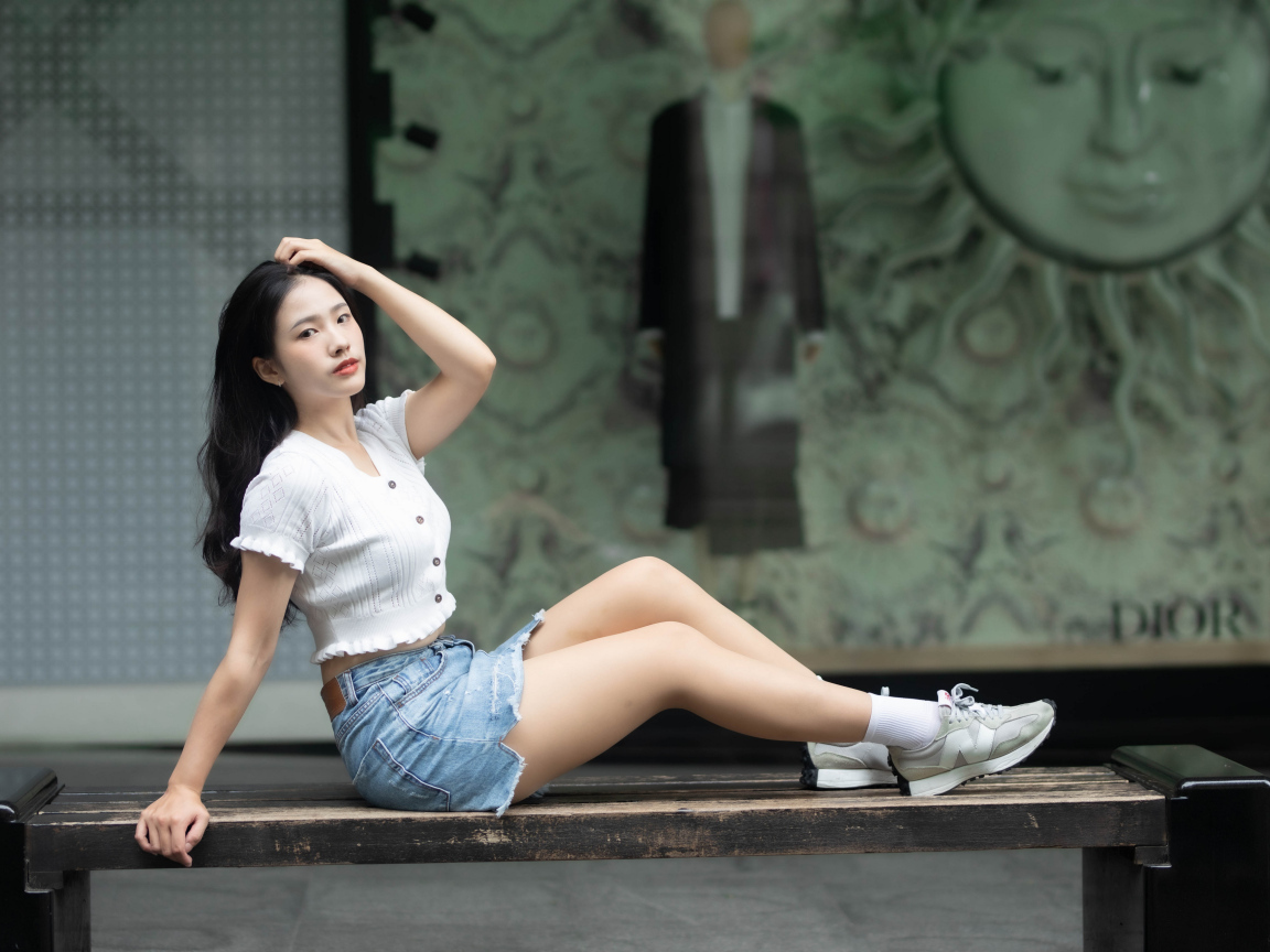 Милая девушка азиатка в белой кофте лежит на лавке