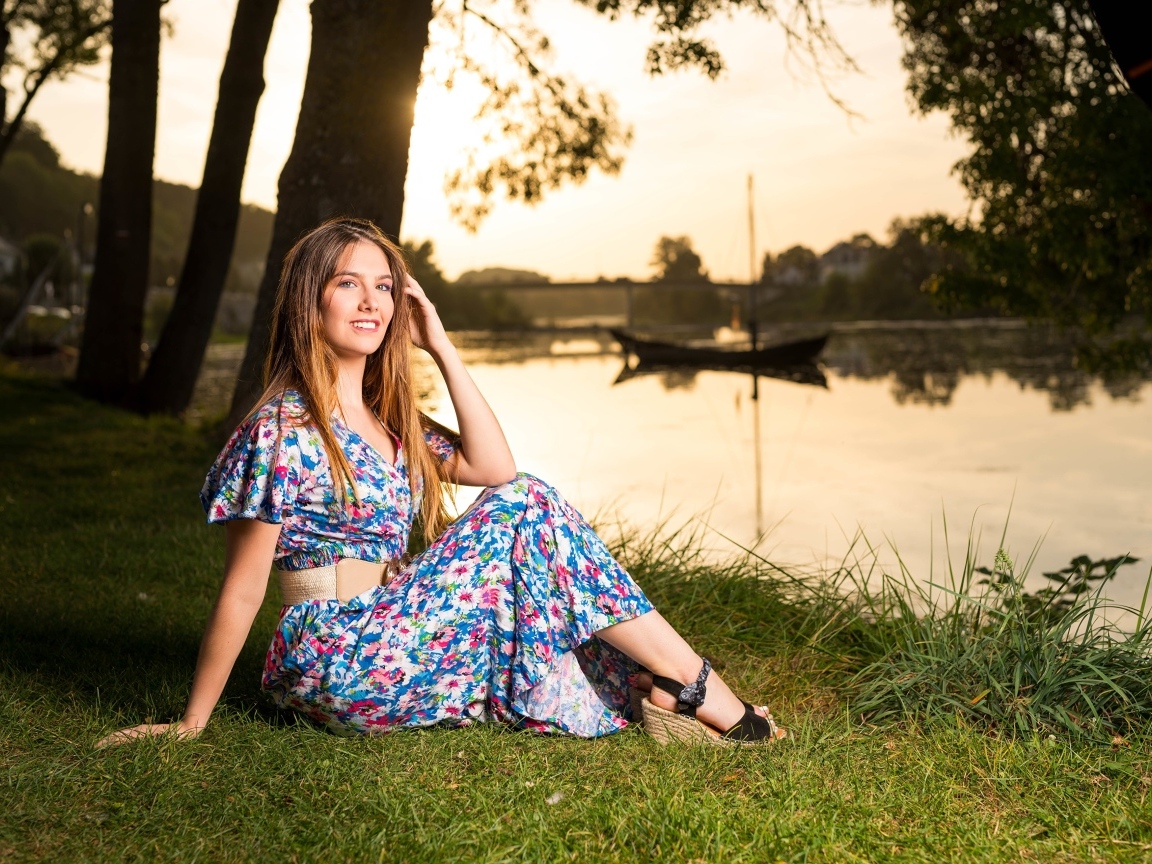 Милая девушка в платье сидит на берегу реки в парке