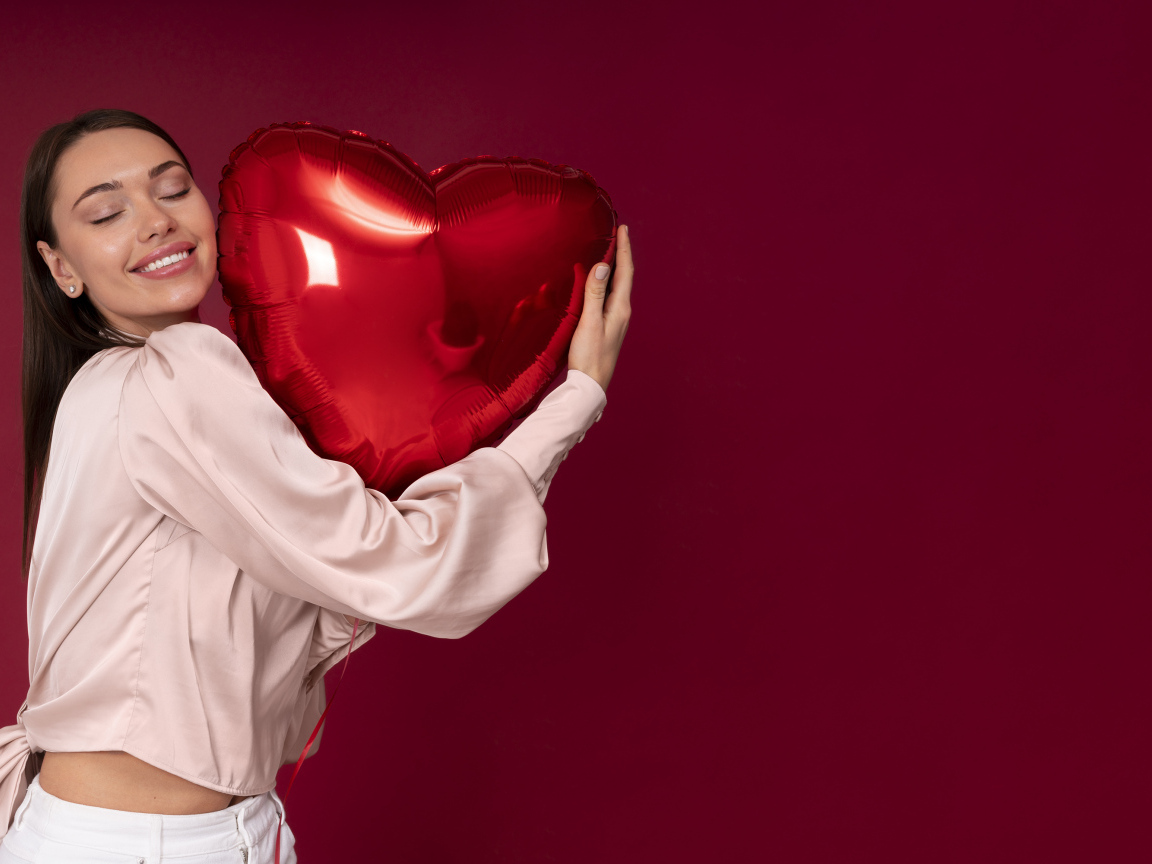 Девушка держит шарик в форме сердца на красном фоне