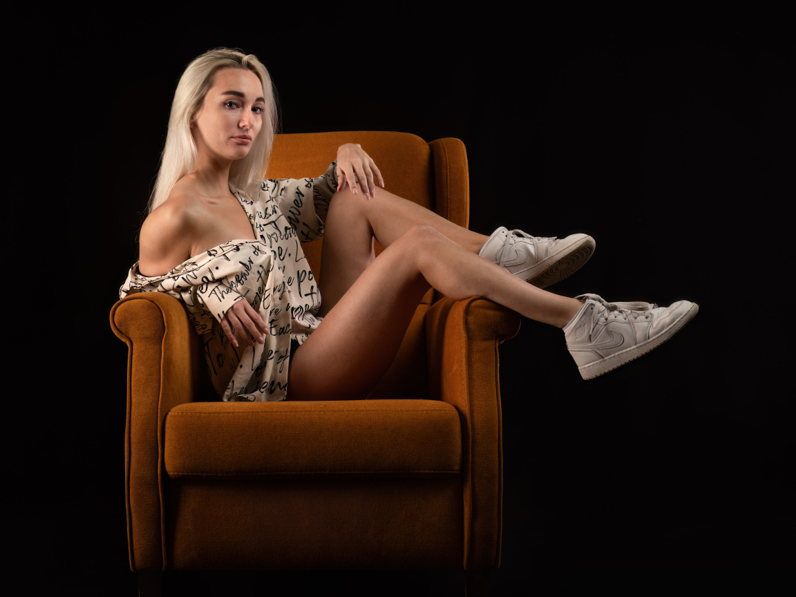 Девушка сидит в коричневом кресле на черном фоне
